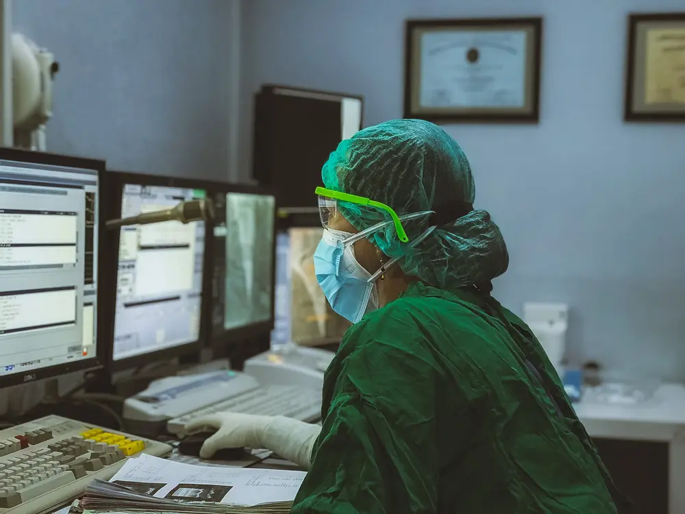 Medical worker focused on digital health records at a busy hospital workstation