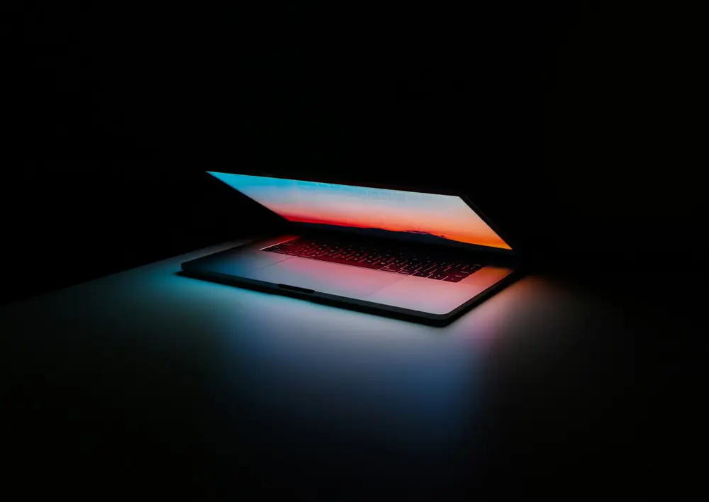 Silver MacBook almost closed on a dark black background
